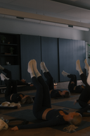 Group of women in navy athleisure sets doing pilates leg raises on mats in a modern studio.