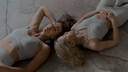 Two women in light grey minimalist athleisure sets posing indoors, wearing sports bras and leggings.